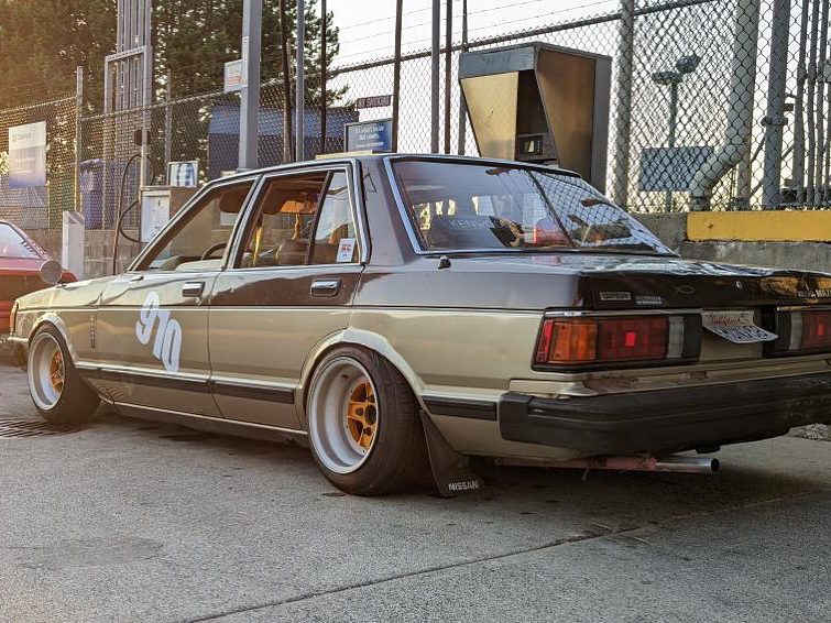 Retro sedan with custom wheels parked at a gas station, sunset lighting enhances vintage vibes.