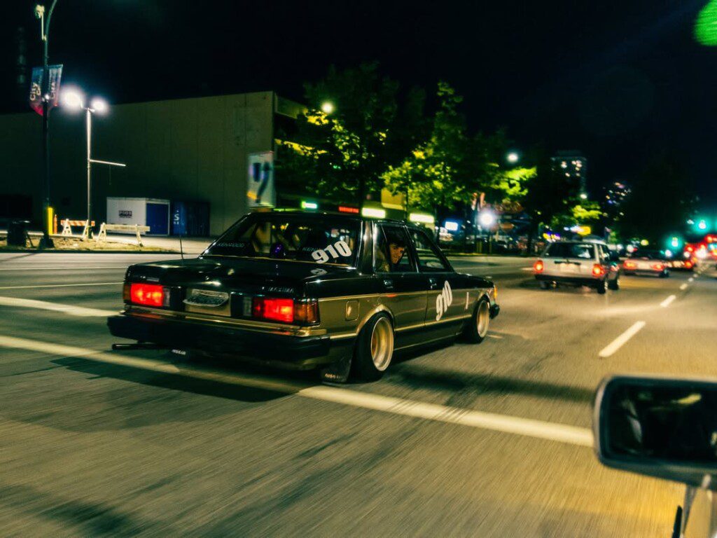 Classic car driving through a lit city street at night, showcasing urban nightlife vibe.