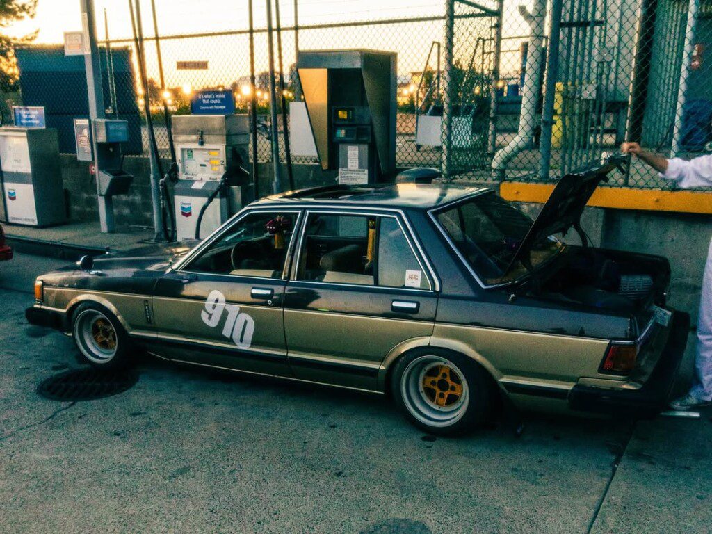 Vintage car with 910 at a gas station, trunk open, at sunset. Classic motor vehicle at fuel pump.