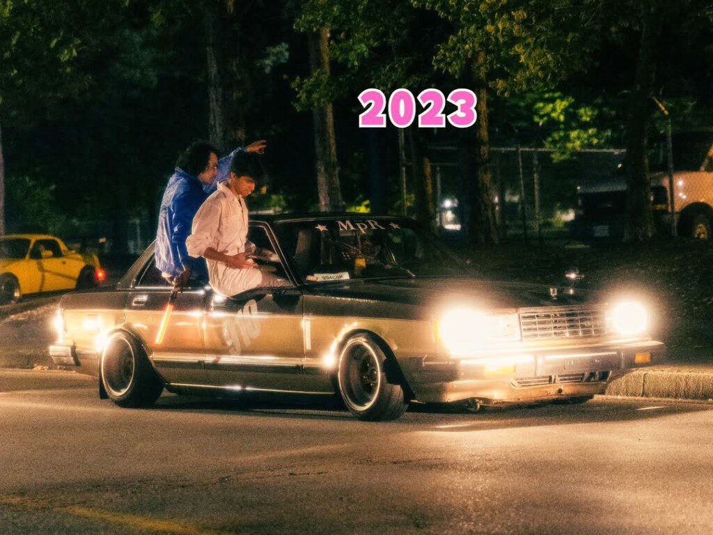 Vintage car with headlights on, people sitting on windows, night street scene, 2023 style.