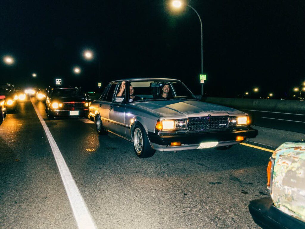 Vintage car cruise on city streets at night, with headlights illuminating the scene.