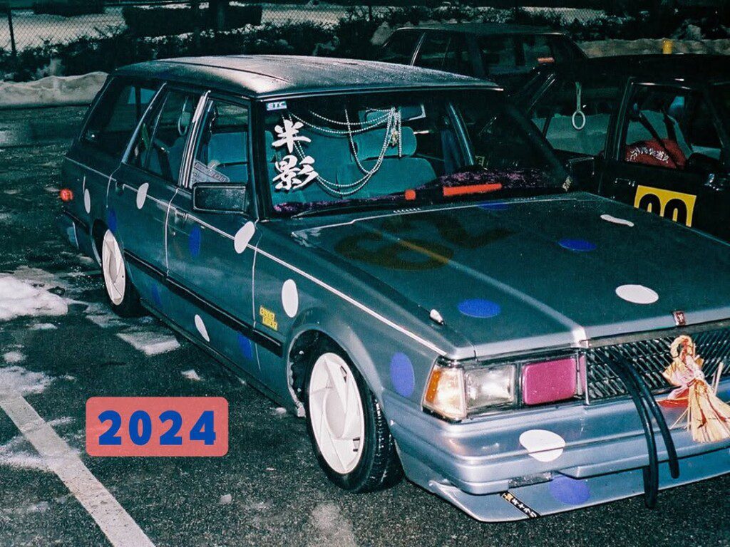 Customized car with polka dot design and 2024 text, parked on a snowy street at night.