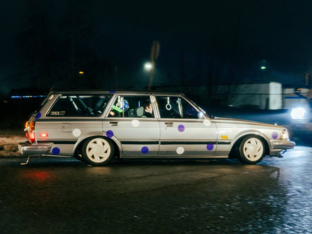 Vintage station wagon with polka dots driving at night, illuminated by streetlights.