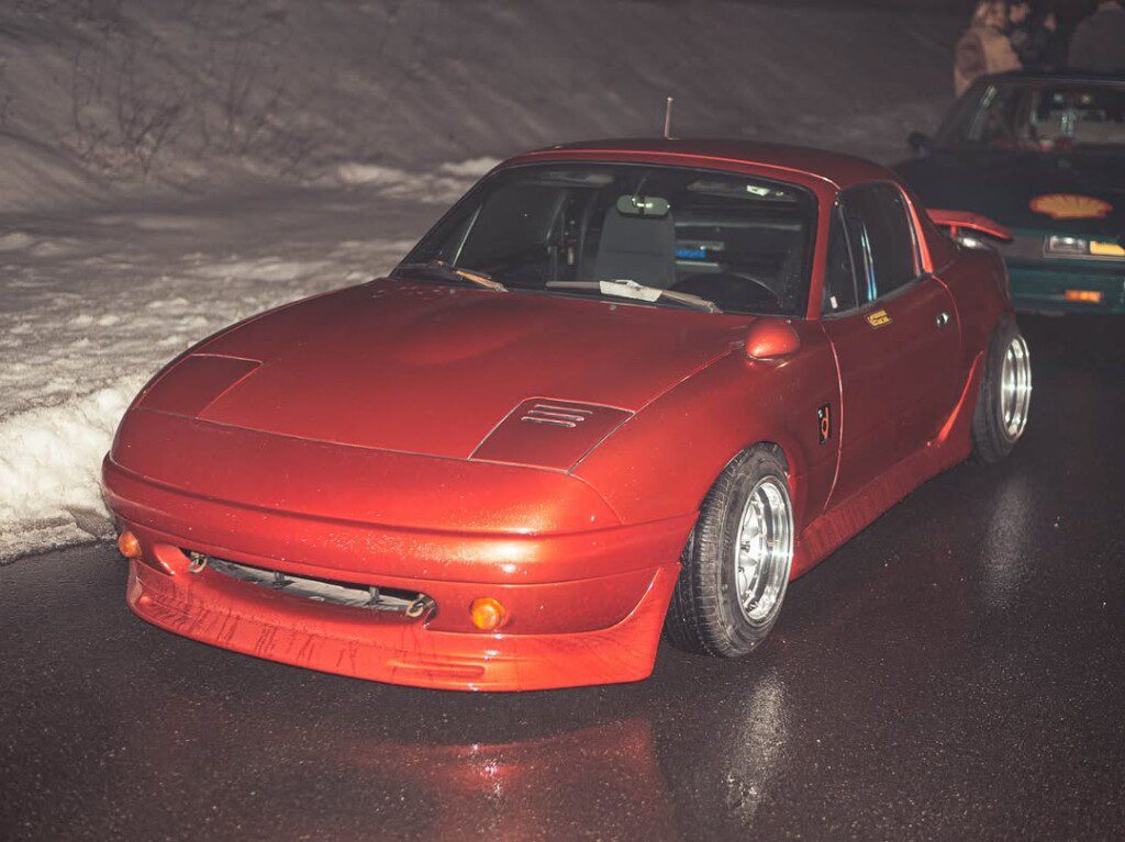 Sleek red sports car on wet road with snowy backdrop, showcasing stylish design and performance at night.