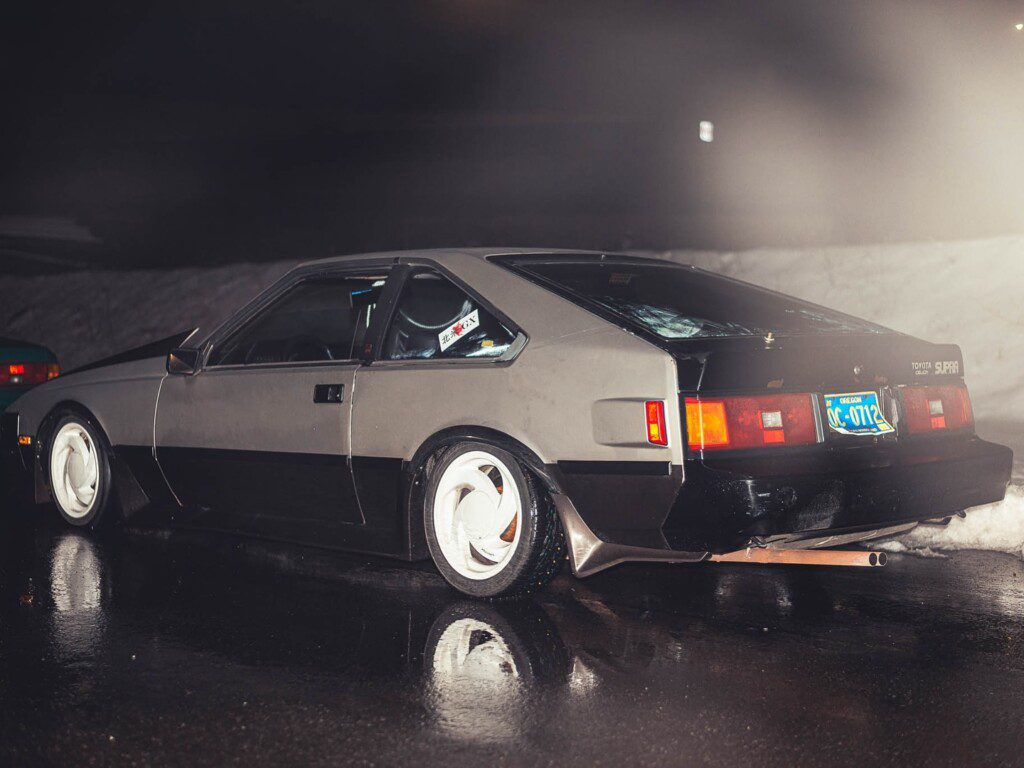 Classic Toyota Supra parked on wet road at night, showcasing sleek design and retro style.