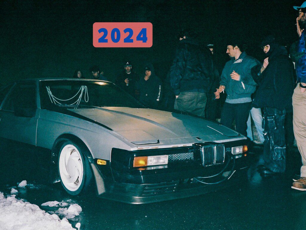 Vintage car at nighttime gathering, surrounded by people, with 2024 text above.