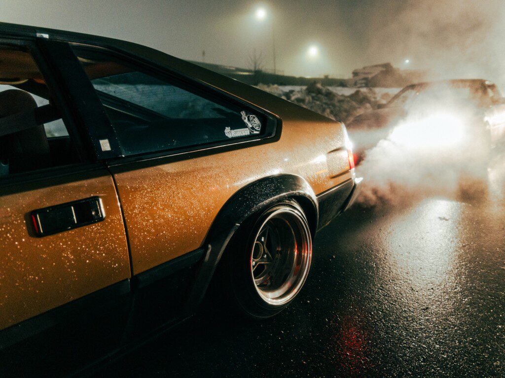 Vintage car with shiny wheels and exhaust smoke in a misty night setting.