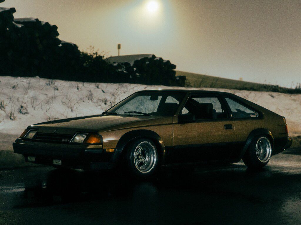 Vintage car parked on a snowy road at night, with a nostalgic glow and a misty background.