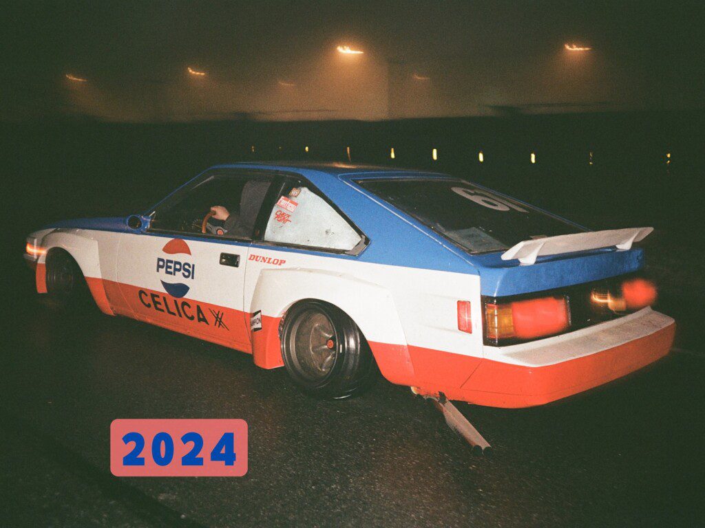 Vintage racing car with Pepsi and Celica decals on a foggy night. Bold 2024 overlay.