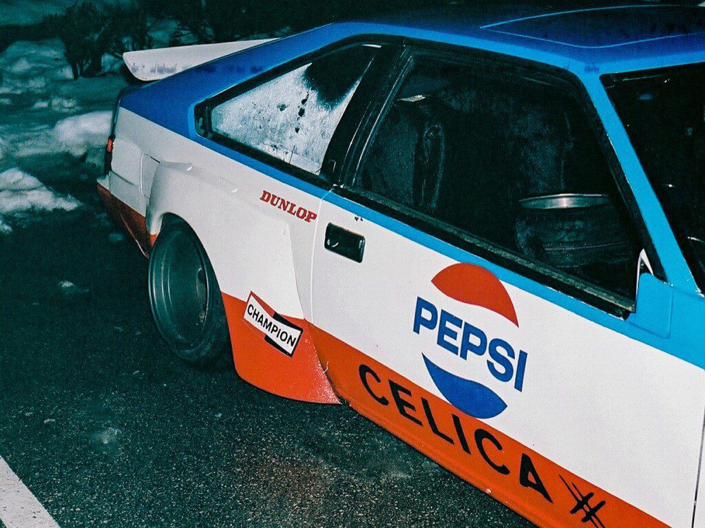 Vintage race car featuring Pepsi and Celica logos with colorful branding parked on a snowy street.