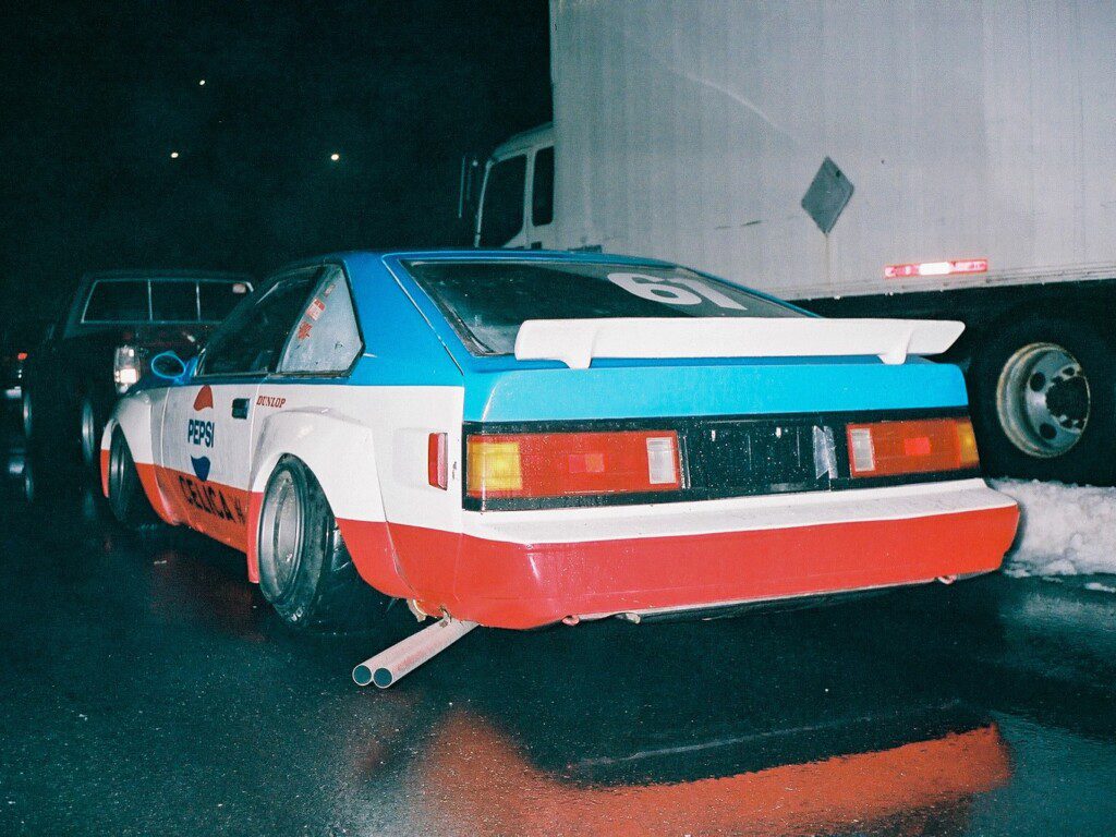 Retro-styled race car with Pepsi branding and custom spoiler parked on wet pavement at night.