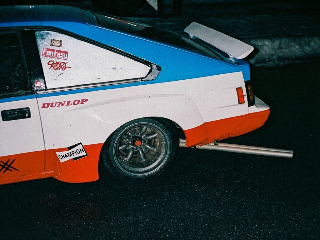 Modified race car with decals, featuring Dunlop branding, parked on a wet road at night.
