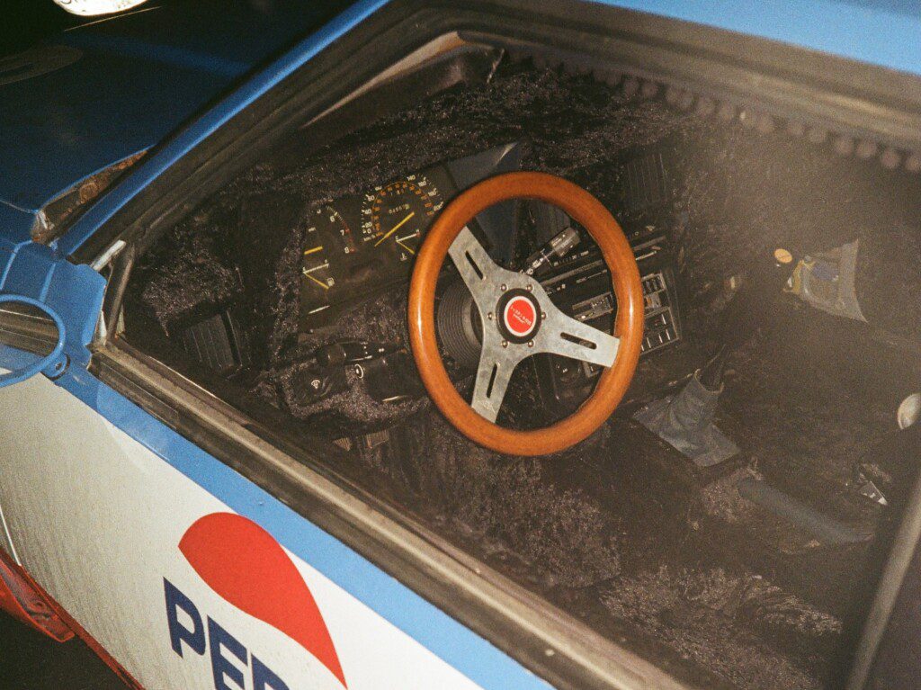 Vintage racing car interior with wooden steering wheel, black textured dashboard, and visible speedometer.