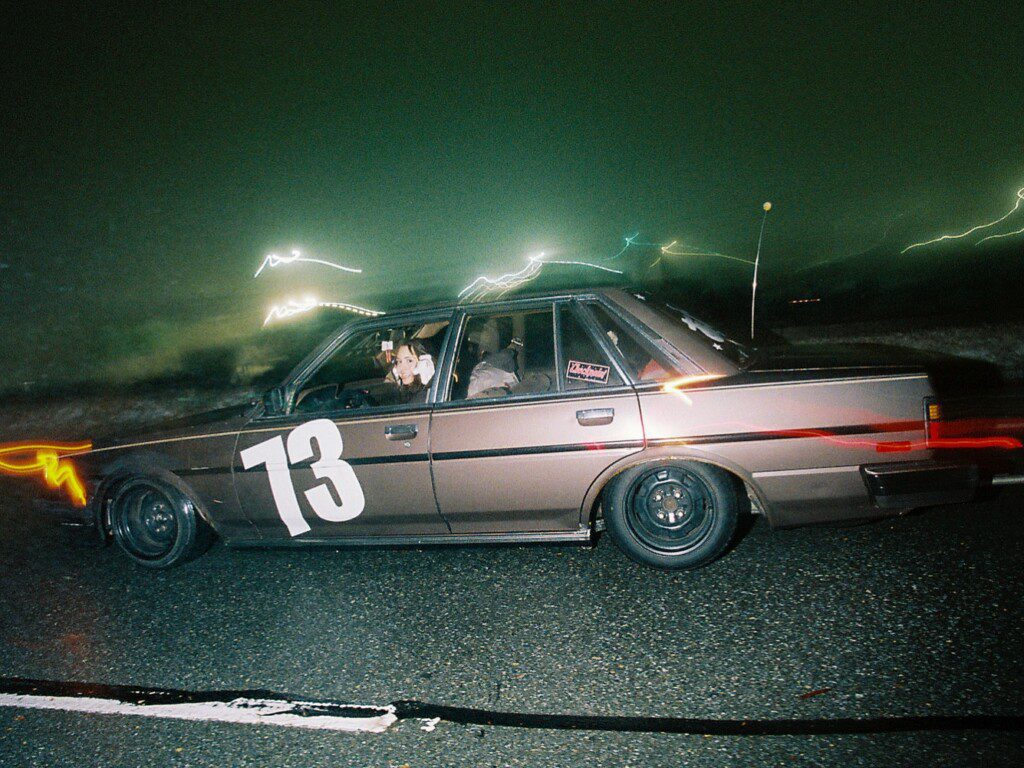 Vintage car with number 73 on door, driven at night under streetlights, capturing motion blur effects.