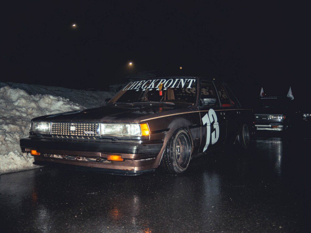 Vintage Toyota race car with Checkpoint decal and number 73, parked on wet pavement at night.
