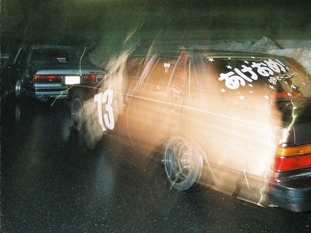 Vintage cars with Japanese text and number 73 on a rainy night, captured with motion blur for a dynamic effect.