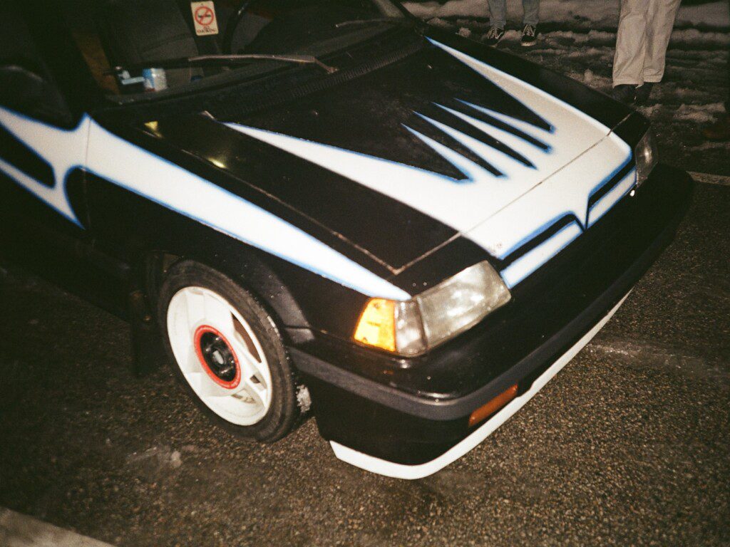 Custom black and white car with unique graphics parked on wet pavement at night.