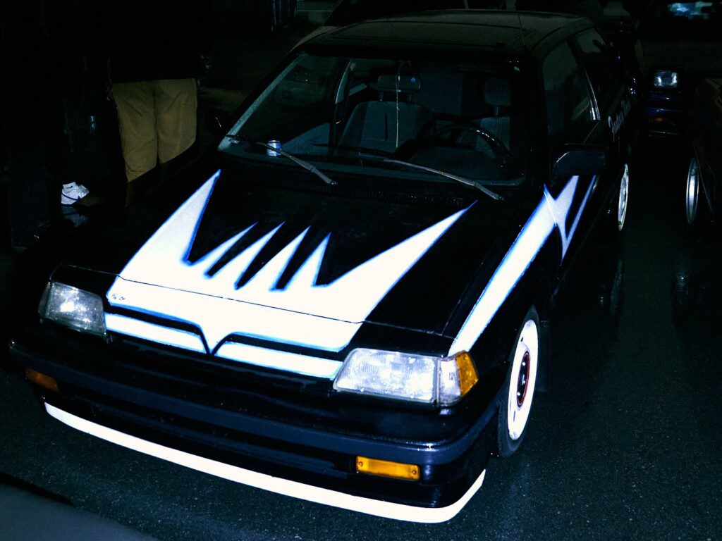 Vintage car with striking white and blue arrow design on hood, parked on a wet street at night.