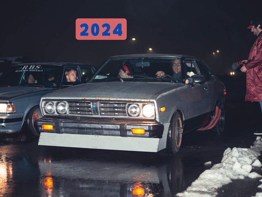 Classic cars at night street race with spectators, 2024 text graphic above.