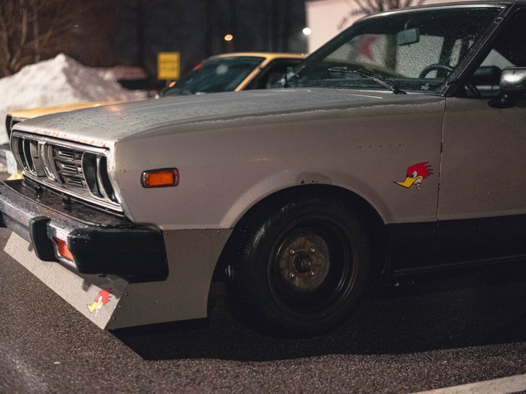 Vintage car with cartoon bird decal, parked on wet asphalt at night.