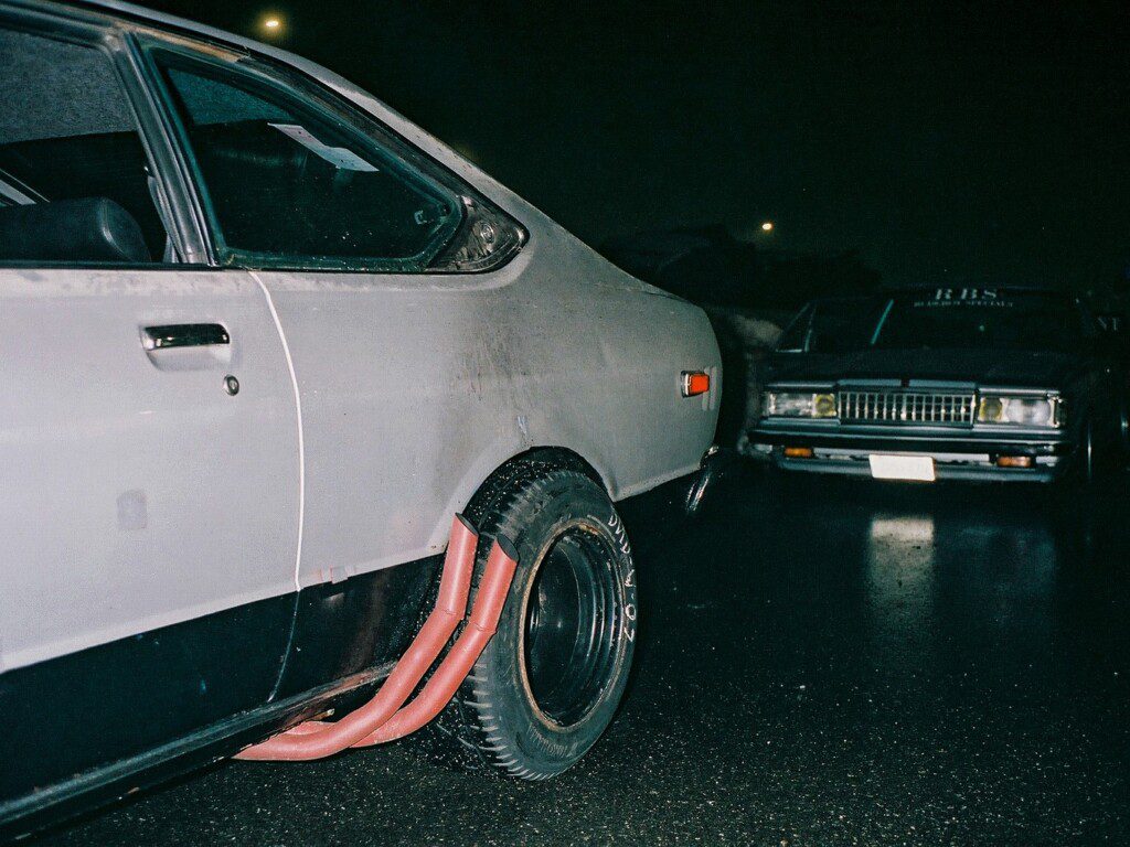 Classic cars parked at night with visible red side exhaust pipes, highlighting vintage automotive design.