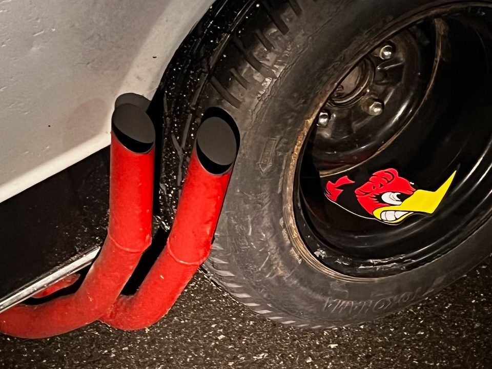 Close-up of red exhaust pipes and a black tire featuring a red cartoon bird decal.