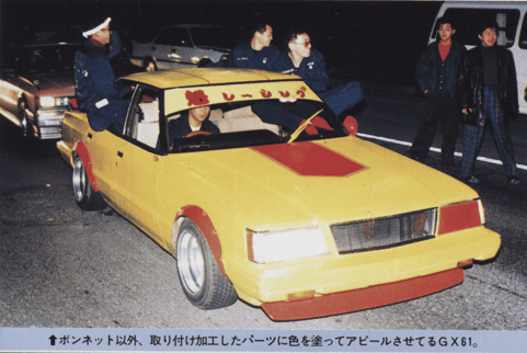 Custom yellow and red modified car at night, surrounded by people in a street setting.