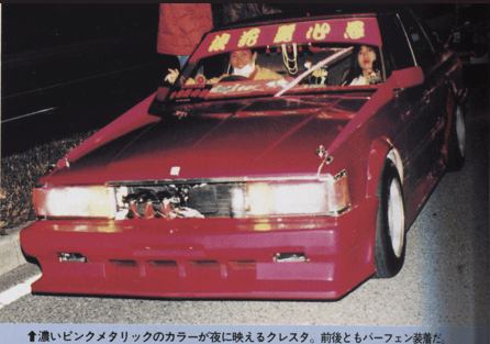 Customized red car with bold front design and decals, parked at night on a street.