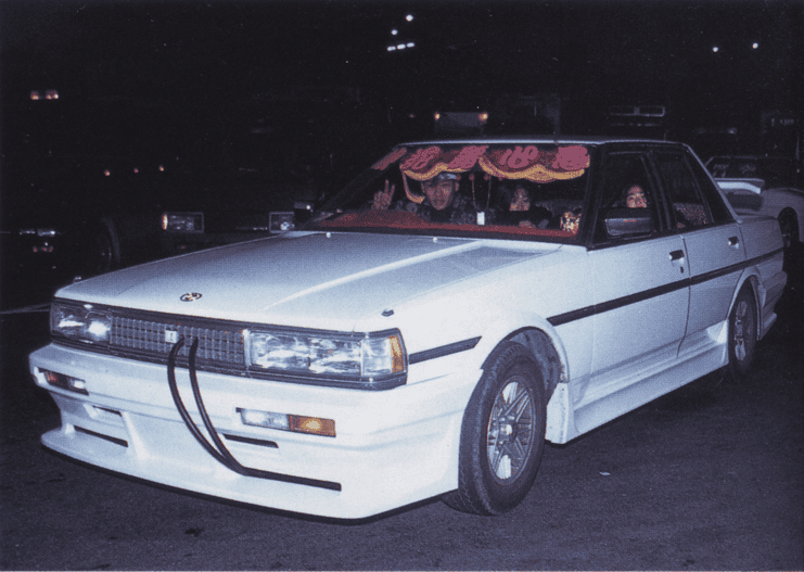 White custom car with decorative windshield and people inside at night.