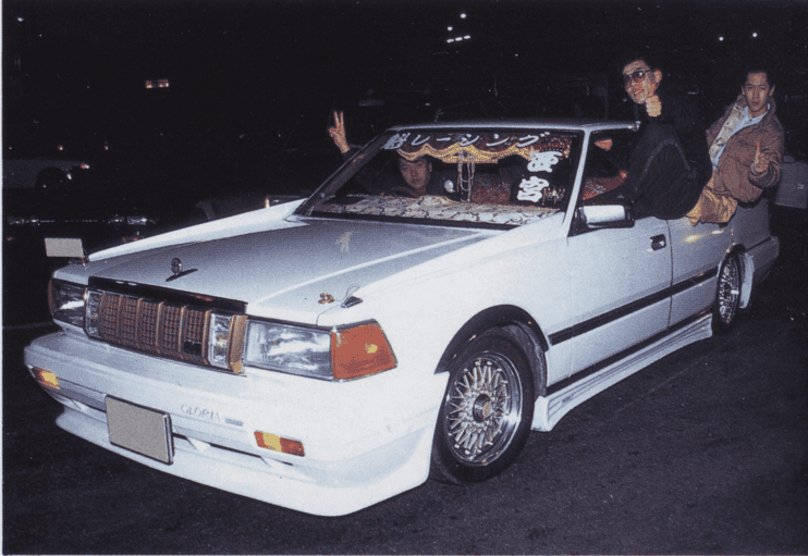 Customized vintage car with unique decals and passengers posing at night.