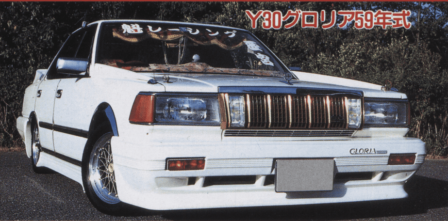 Classic modified Y30 Nissan Gloria in white, showcasing a bold front grille and custom wheels, parked on a sunny day.