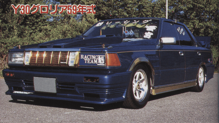 Vintage modified blue sedan with decals, showcased on a sunny day, emphasizes custom auto design and racing team.