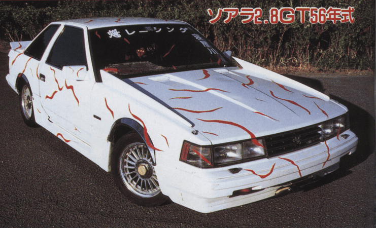 White retro car with red accents and black-tinted windows parked on a road, featuring vintage 1980s Japanese styling.