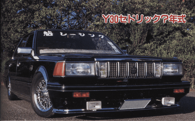 Black Y30 Sedan with chrome grille and wheels parked outdoors next to greenery.