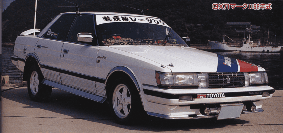 Vintage white Toyota sports car with custom decals, parked by the waterfront.