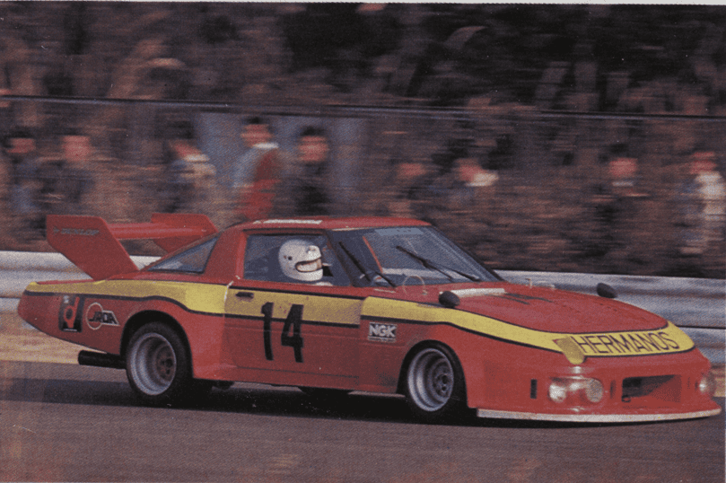 Race car number 14, red and yellow, speeds on track with blurred background, showcasing motorsport action.