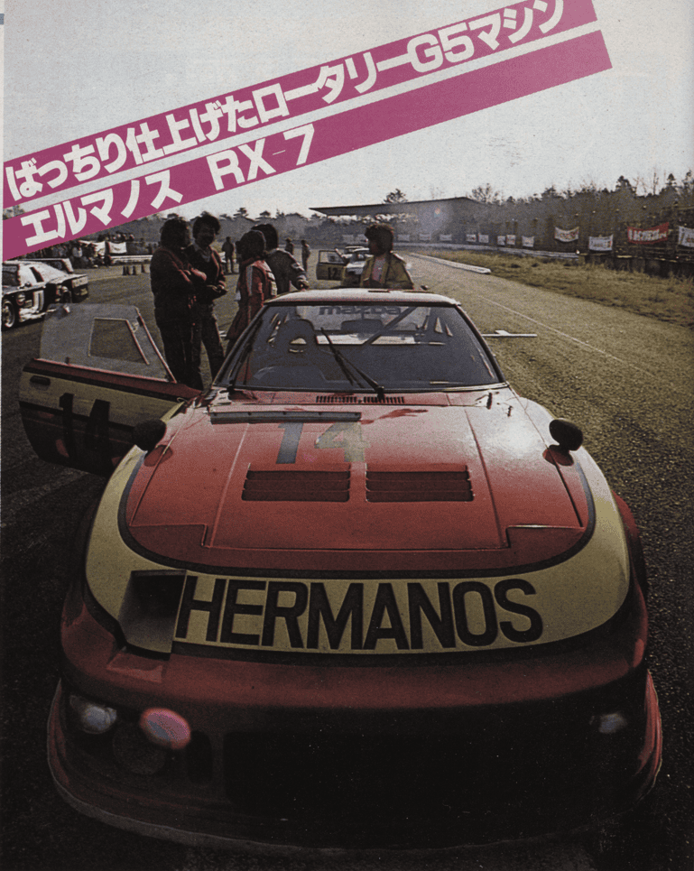 Vintage race car Mazda RX-7 on track, ready for competition, with crew members and spectators in the background.