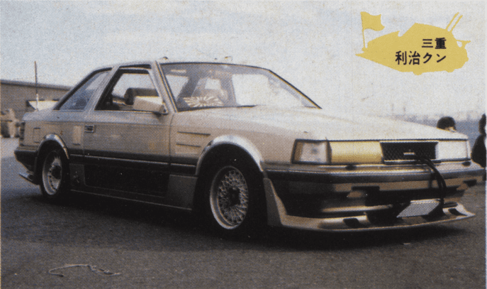 Vintage customized car with body kit and aftermarket wheels parked outdoors.