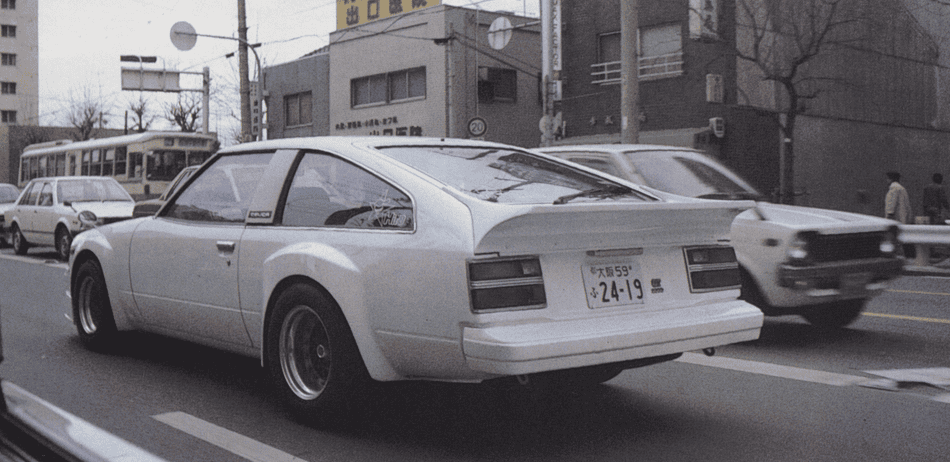 Vintage white sports car driving in urban street setting, showcasing classic automotive design.