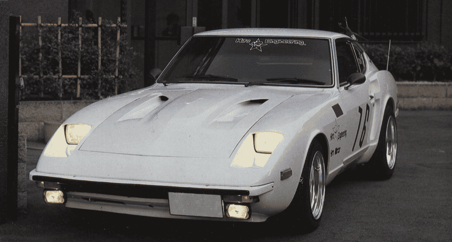 White classic sports car with decals parked in front of a building, showcasing vintage design and sleek styling.