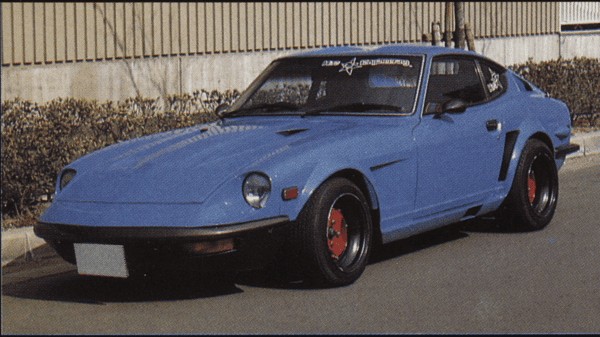 Vintage blue sports car with sleek design and red rims parked on a street, showcasing classic automotive style.