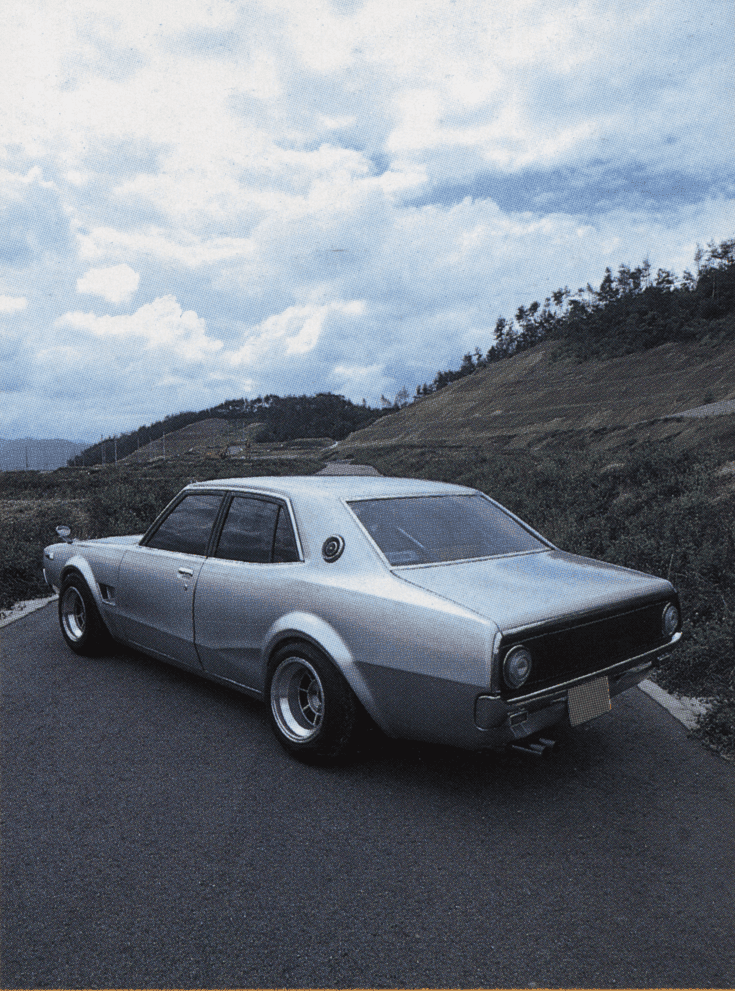 Vintage silver car parked on a scenic road with a cloudy sky backdrop.