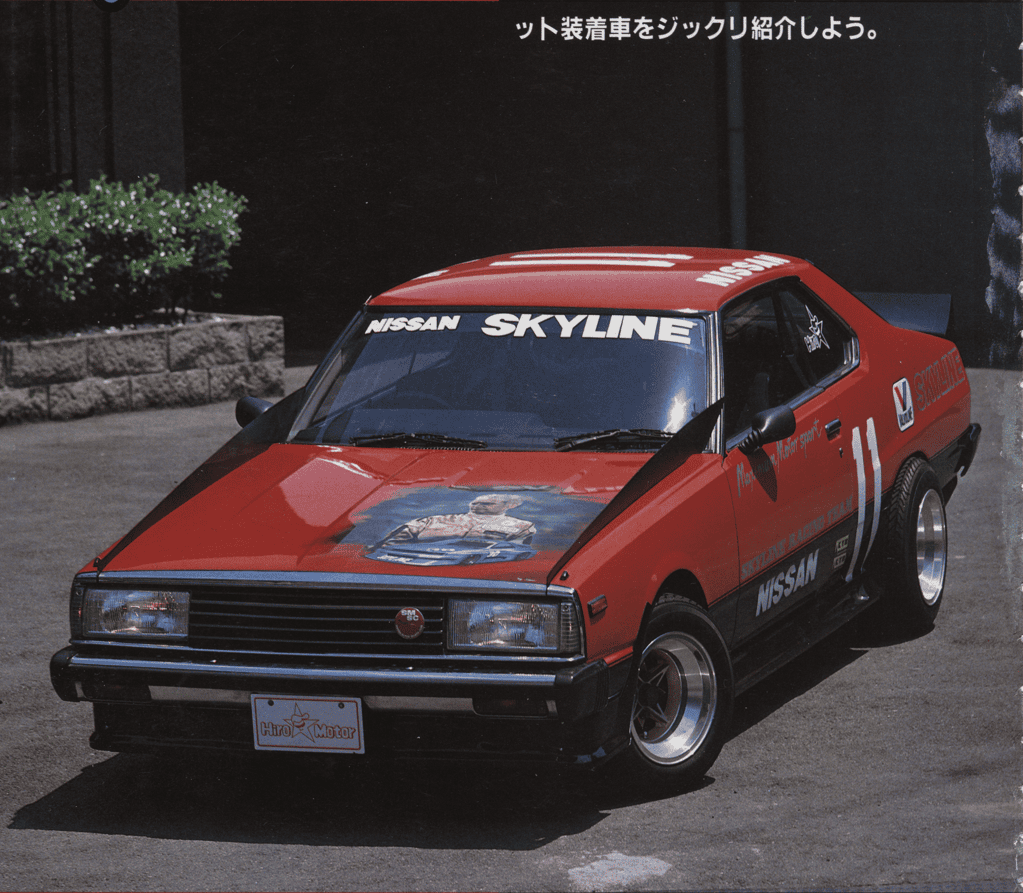 Red Nissan Skyline race car with custom hood art and decals, parked on a street, showcasing sporty design.