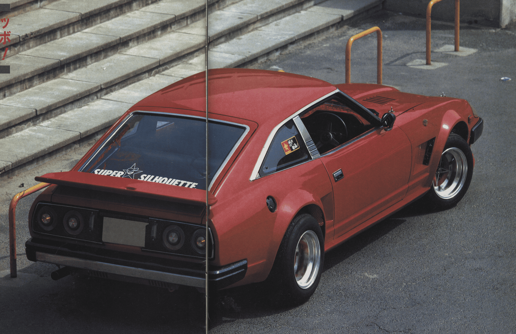 Red vintage sports car parked near steps with Super Silhouette decal on rear window, angled view.