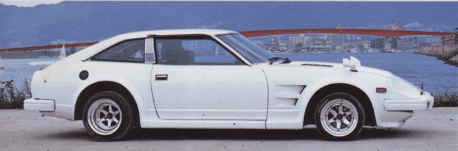 Vintage white sports car parked by a scenic coastal bridge with hills in the background.