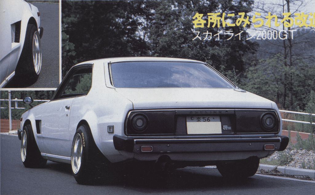 Vintage white car parked on a road, viewed from the rear, showcasing classic design and stylized wheels.