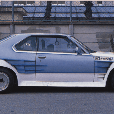 Side view of a custom retro car with sporty body kit, parked on a street with trees in the background.