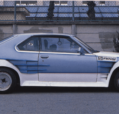 Side view of a custom retro car with sporty body kit, parked on a street with trees in the background.