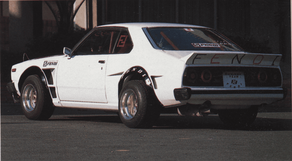 Classic white sports car with custom modifications and FENOL branding, parked in an urban setting.