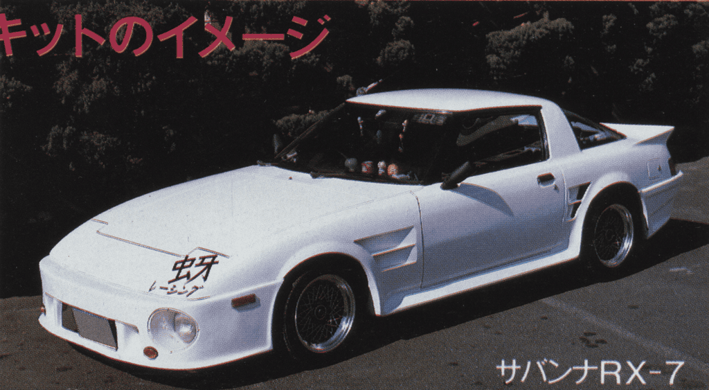 White custom Mazda RX-7 with aerodynamic body kit, parked outdoors on a sunny day.